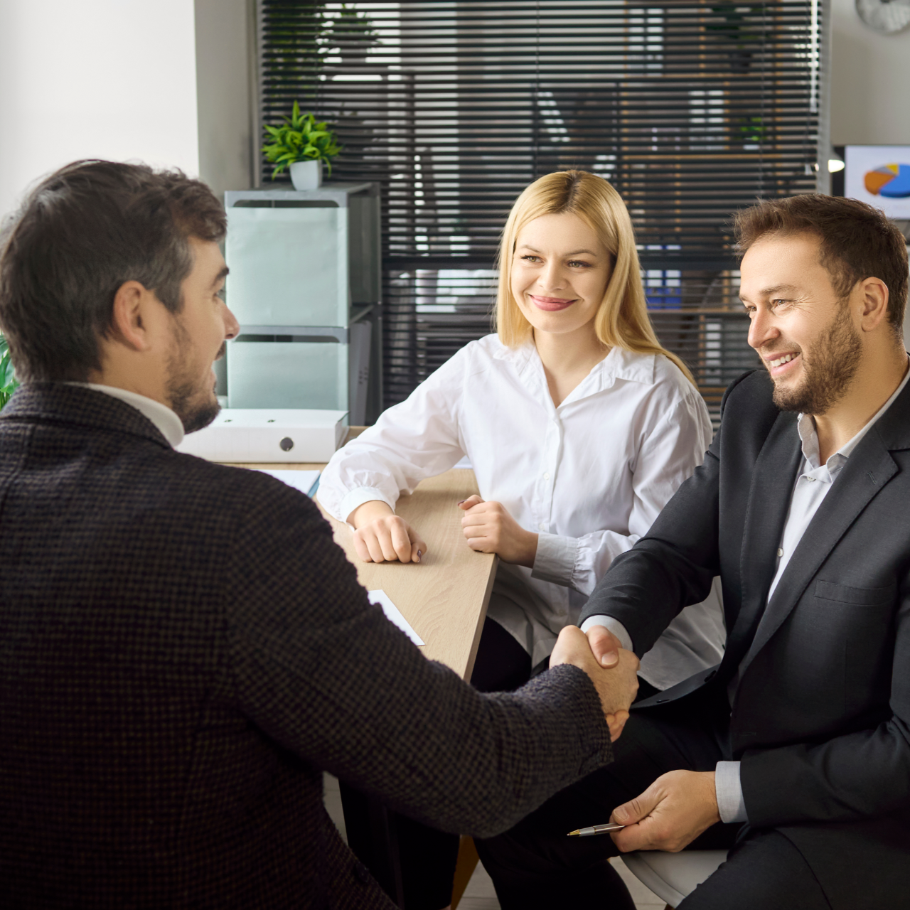 Business meeting with three people shaking hands and smiling in a bright office
