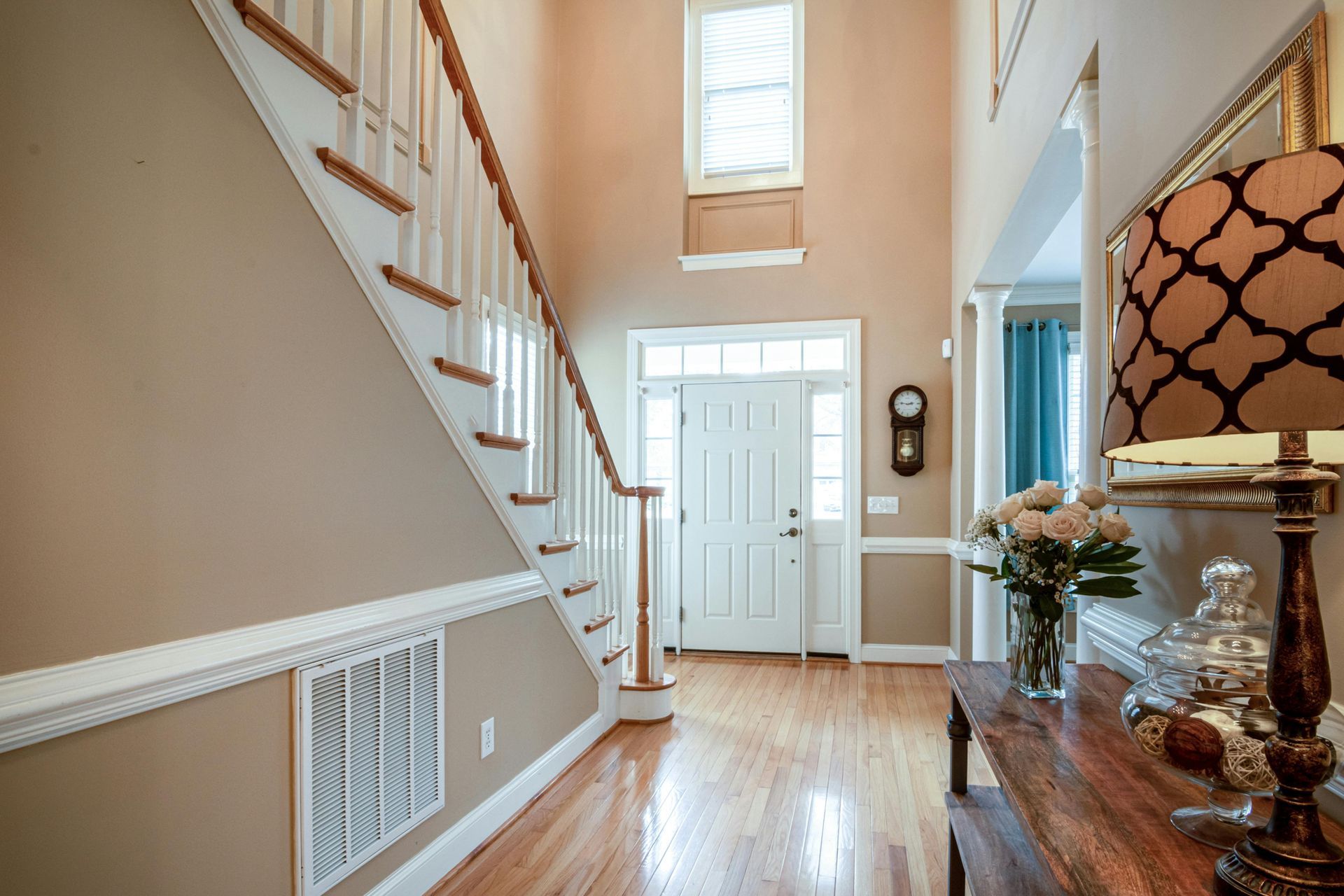 Bright entry hall with staircase, white front door, and wooden floor, lit by a window.