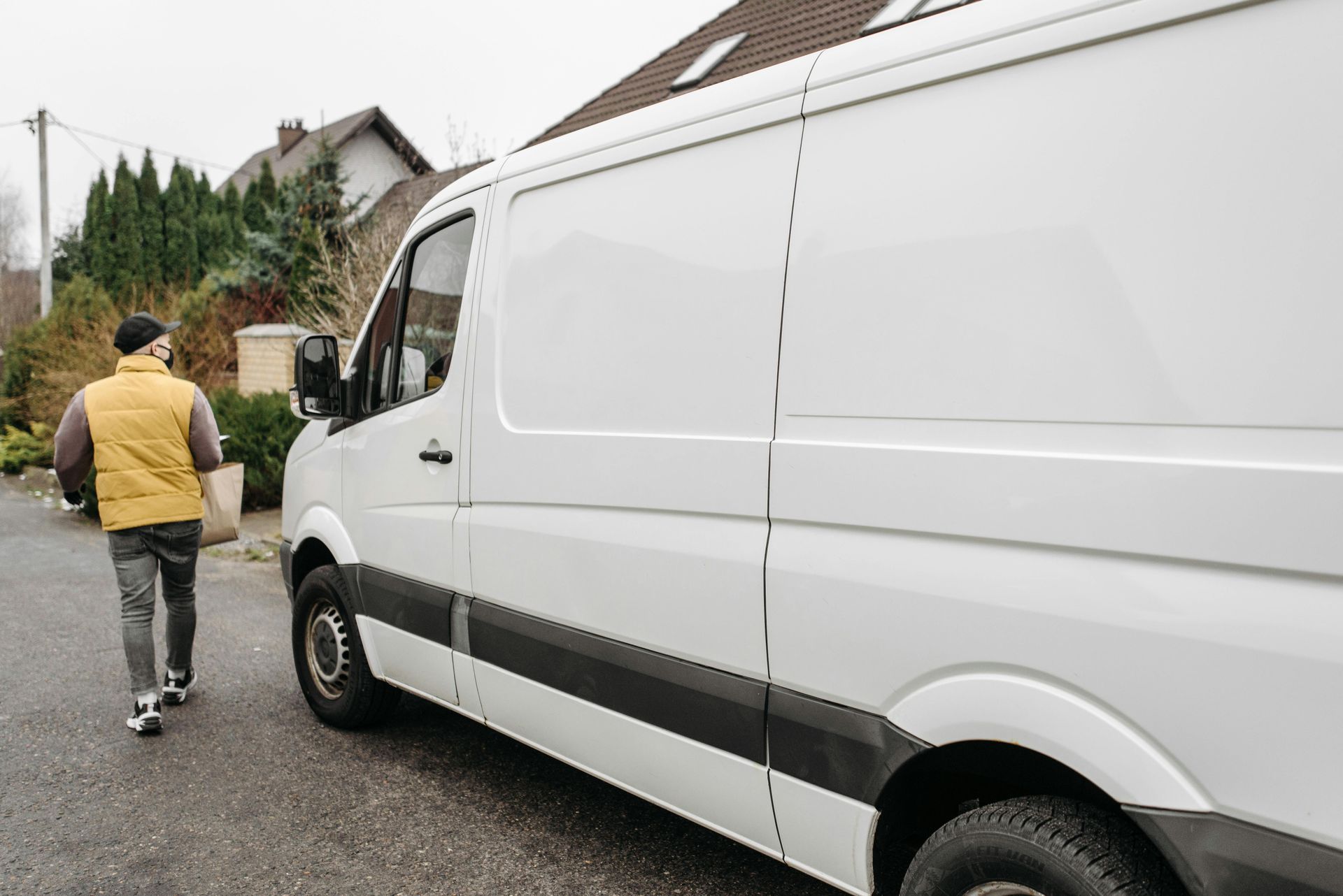 Person walking beside a white cargo van on a residential street.