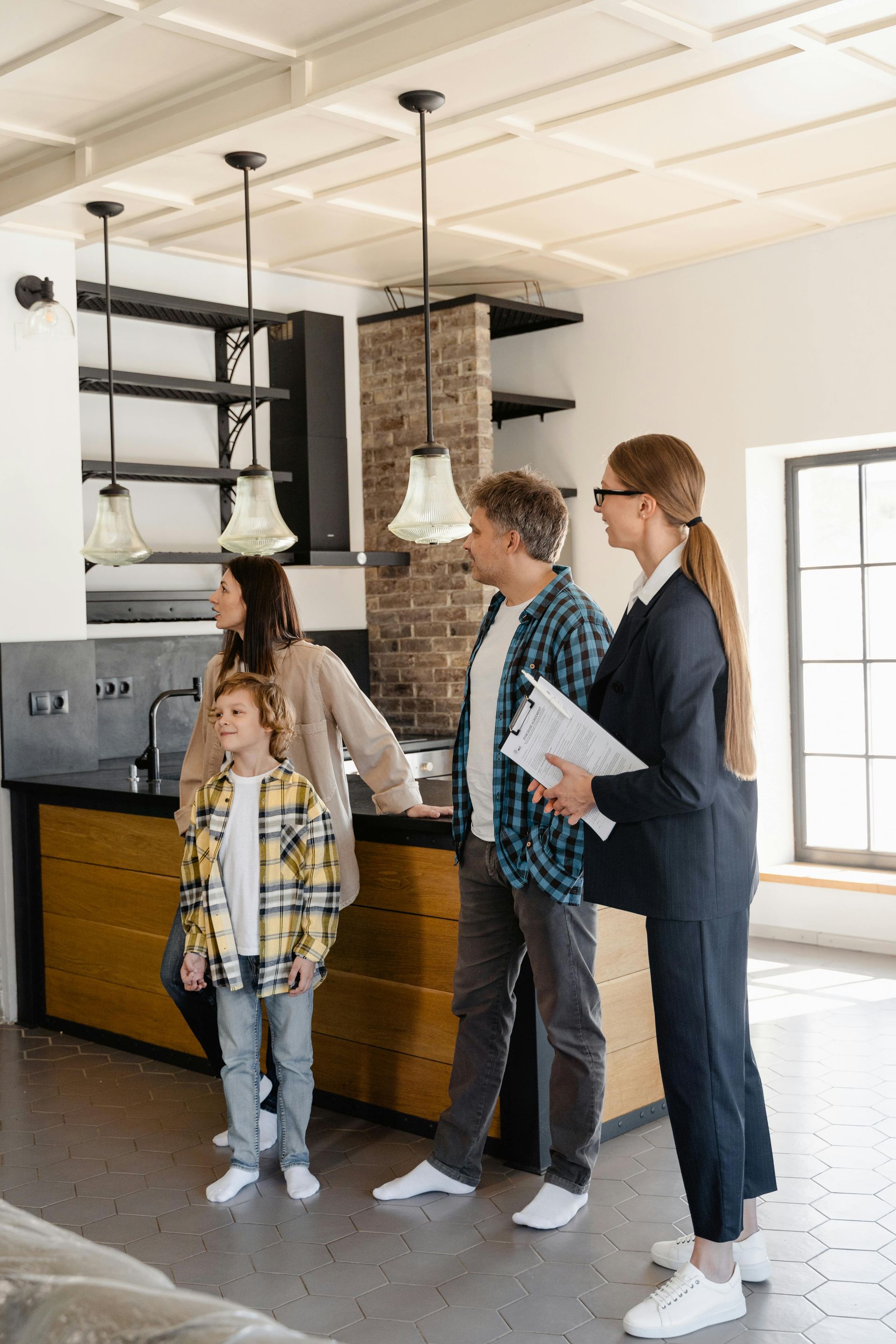 Four people stand in a bright room with pendant lights, looking at wood cabinets and shelving.