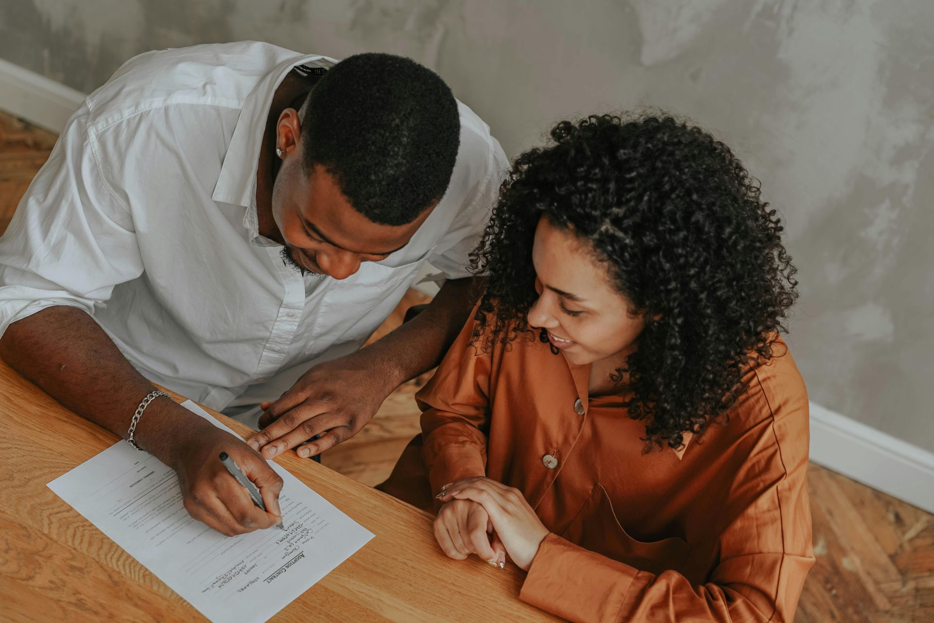 Two people reviewing paperwork together at a table, one writing with a pen.