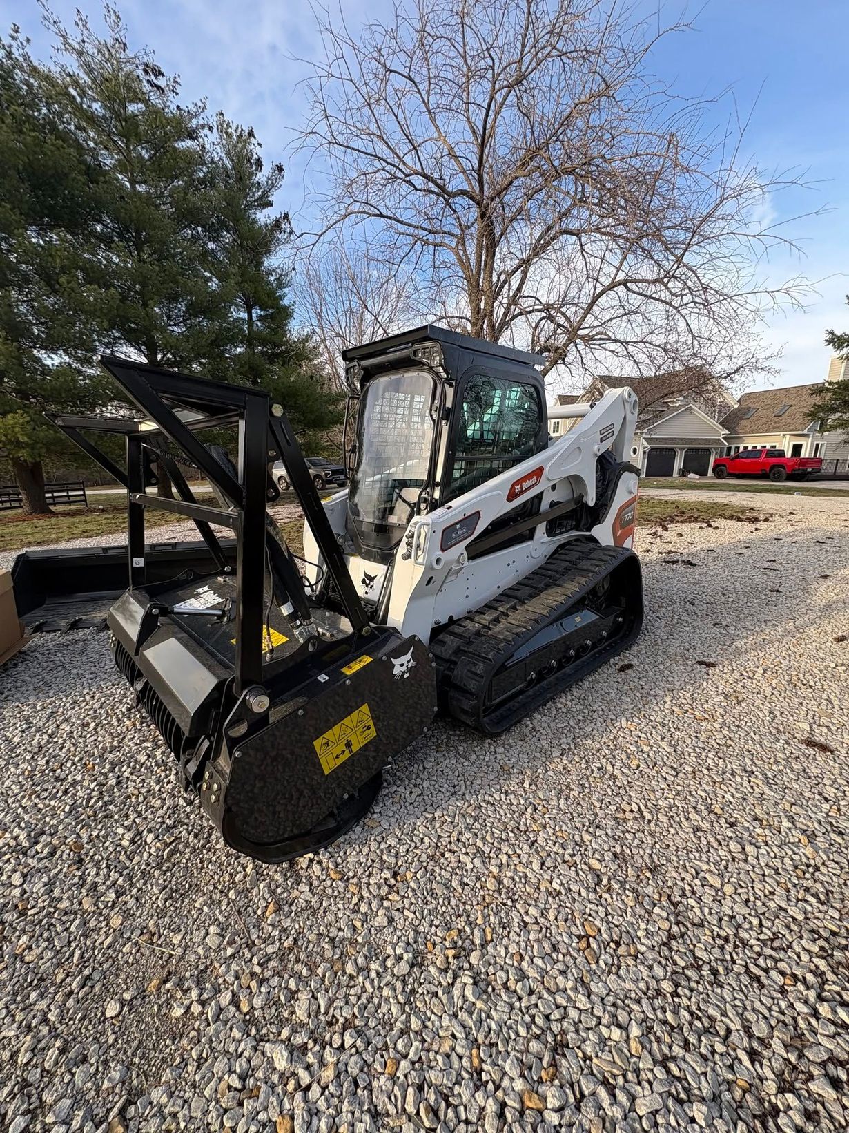 White Bobcat skid steer with front grapple parked on gravel under a blue sky