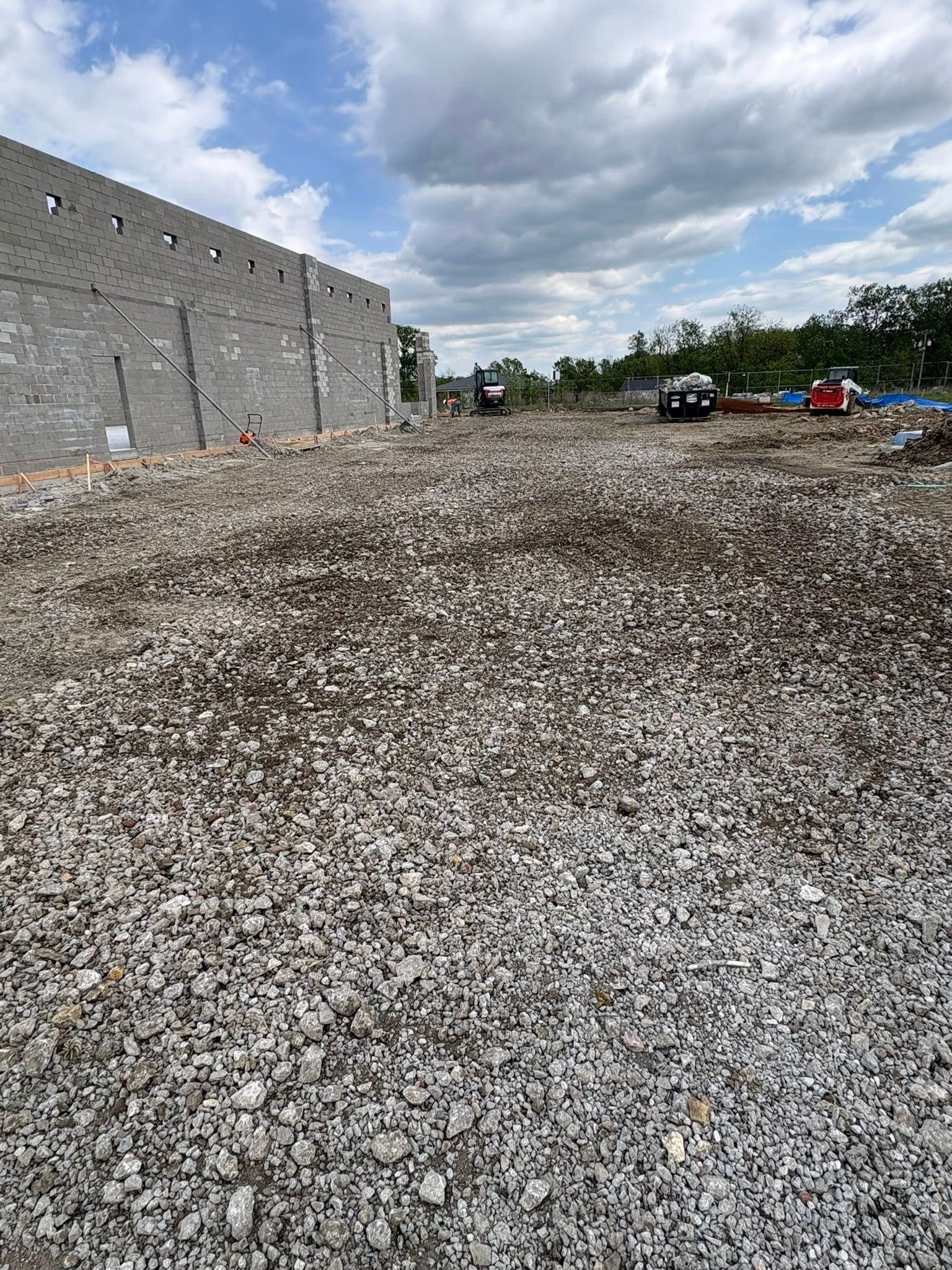 Gravel lot beside a stone building under cloudy sky, with a few parked vehicles in the distance.