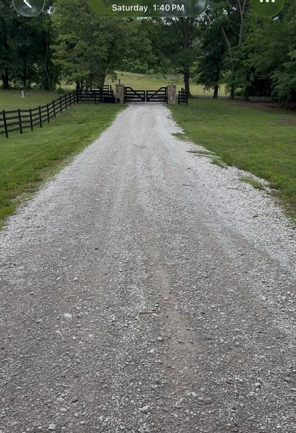 Gravel driveway leading to a wooden gate in a green, tree-lined yard.