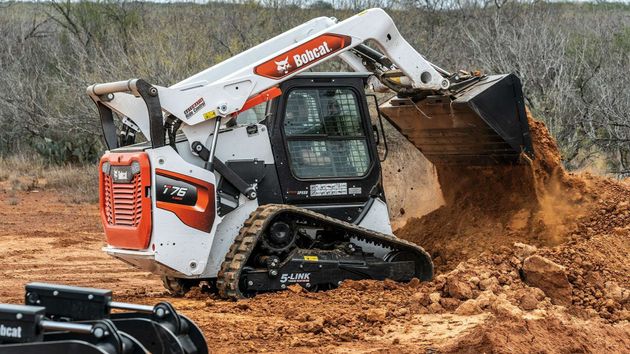 White Bobcat skid-steer loader digging dirt at a muddy construction site