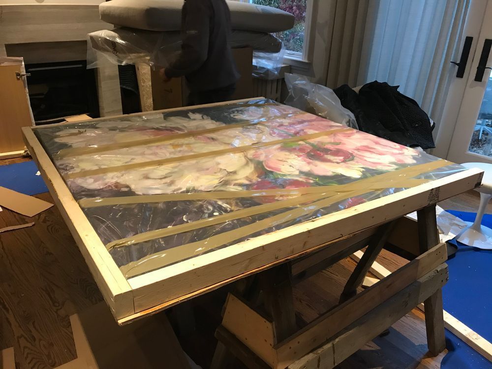 Large painting wrapped in plastic on a wooden stand in a room, ready for moving.