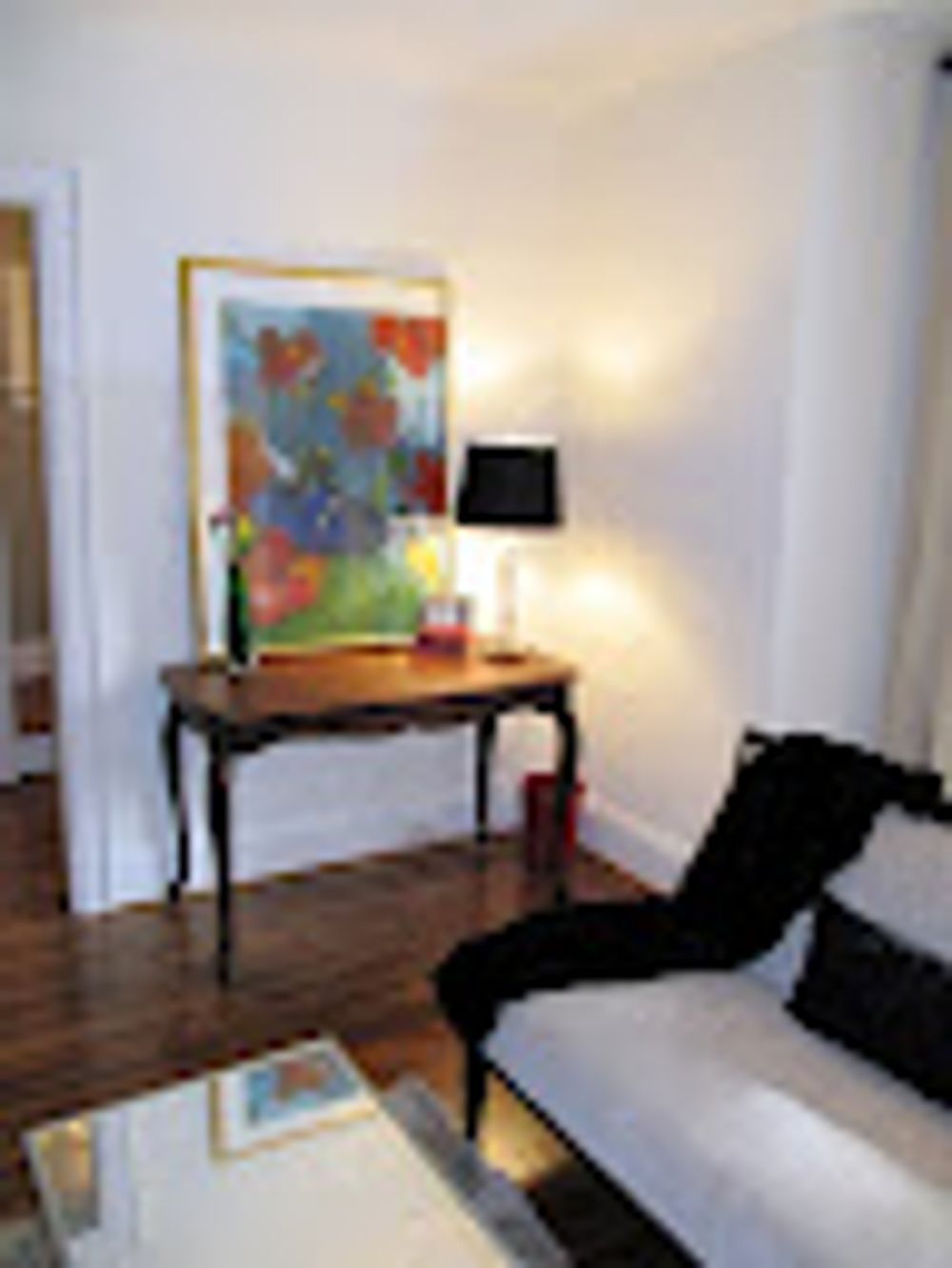 Living room corner with a console table holding art, lamp, and couch covered with a black throw.