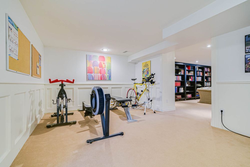 Home gym with exercise bikes, rowing machine, weight bench, and bookshelves.