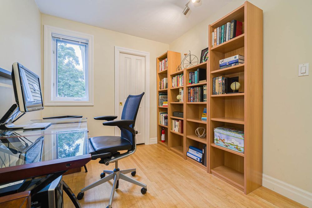 Home office with desk, chair, and bookshelves; window, door, and hardwood floor.