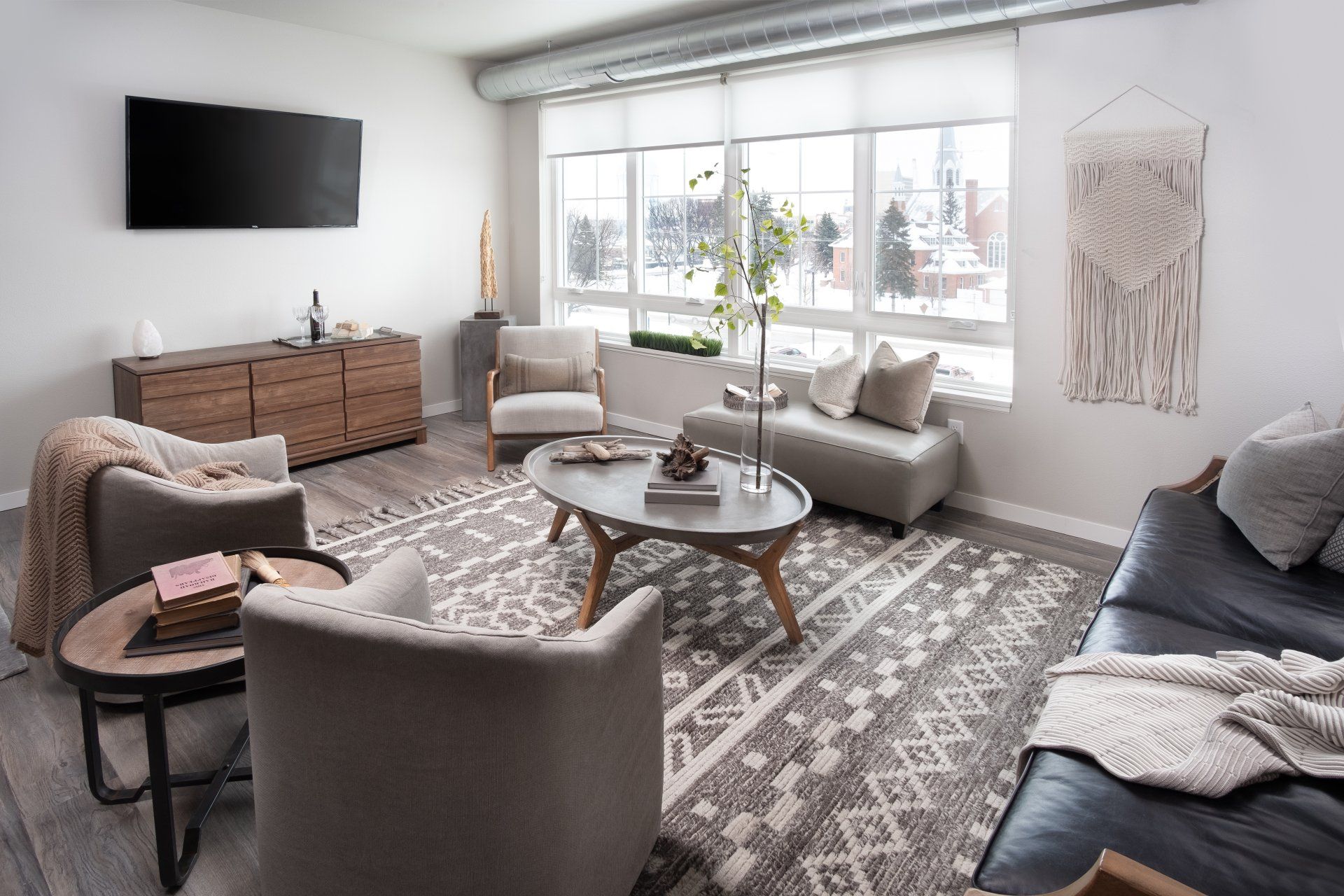 Light and bright living room of 2nd floor apartment with TV on the wall, large windows, and modern living room furniture.