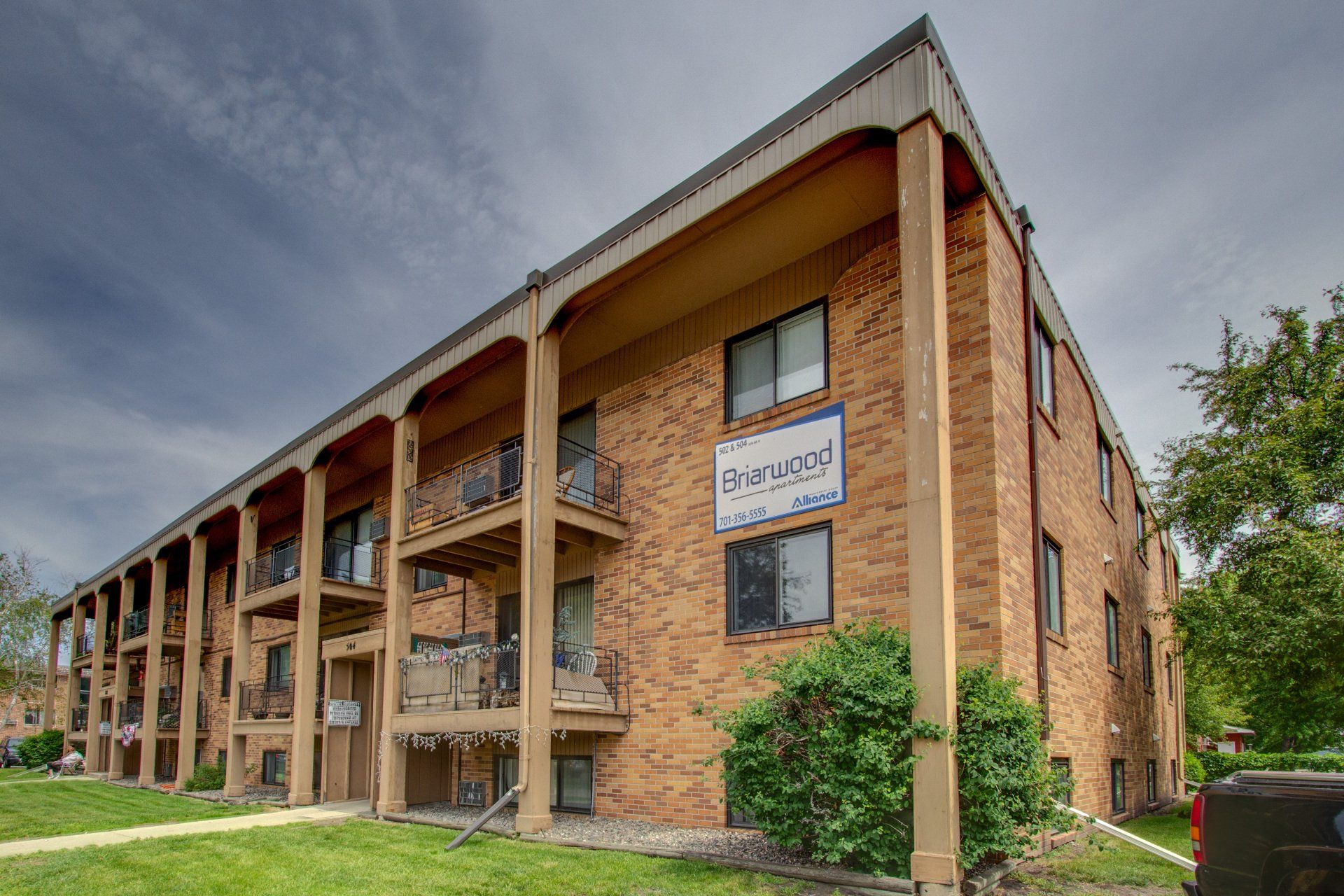 Older brown brick building, with a white and blue sign on the front corner that says Briarwood and a cloudy blue sky.