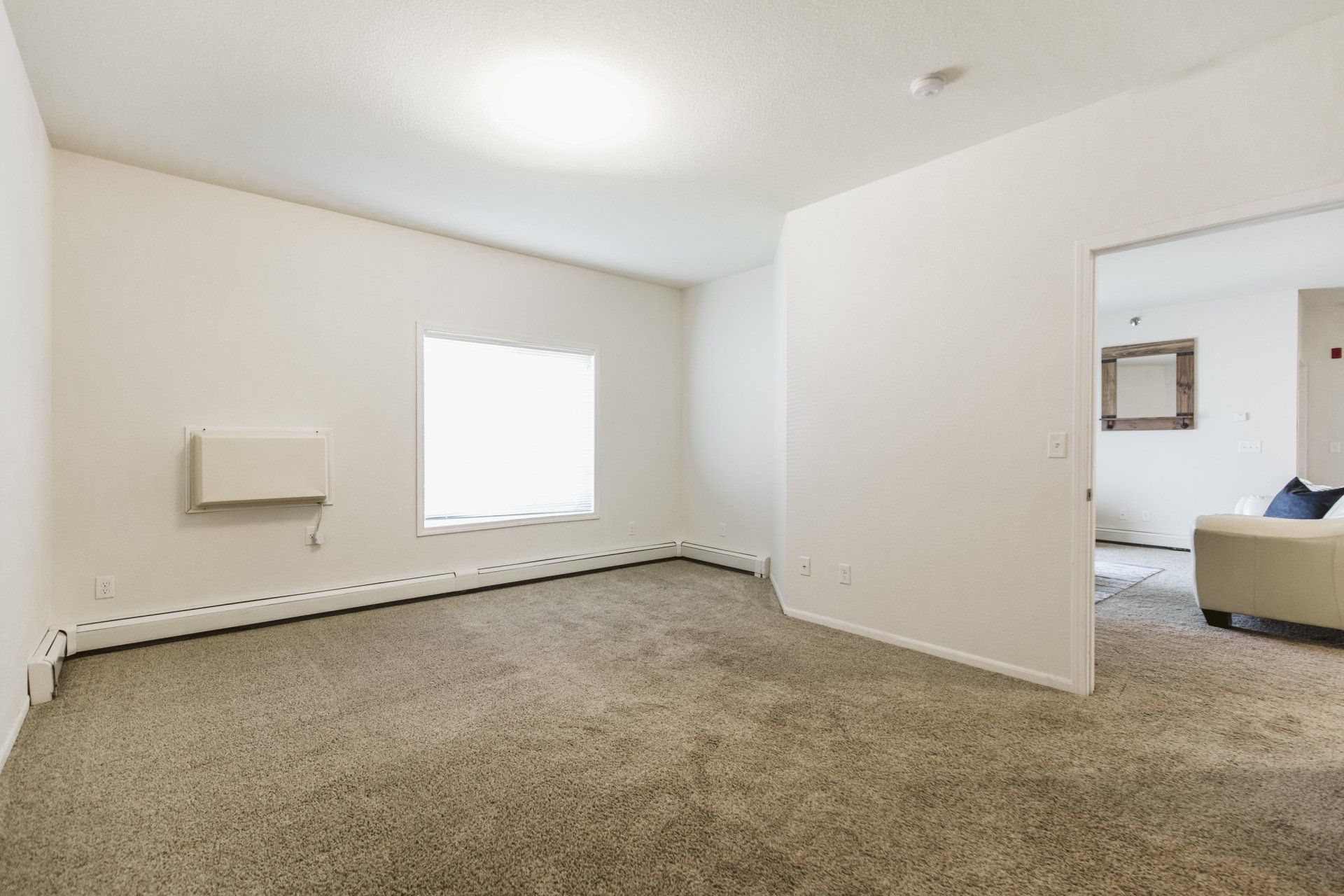 Carpeted bedroom with large window and wall A.C. unit, doorway leading to kitchen and living room