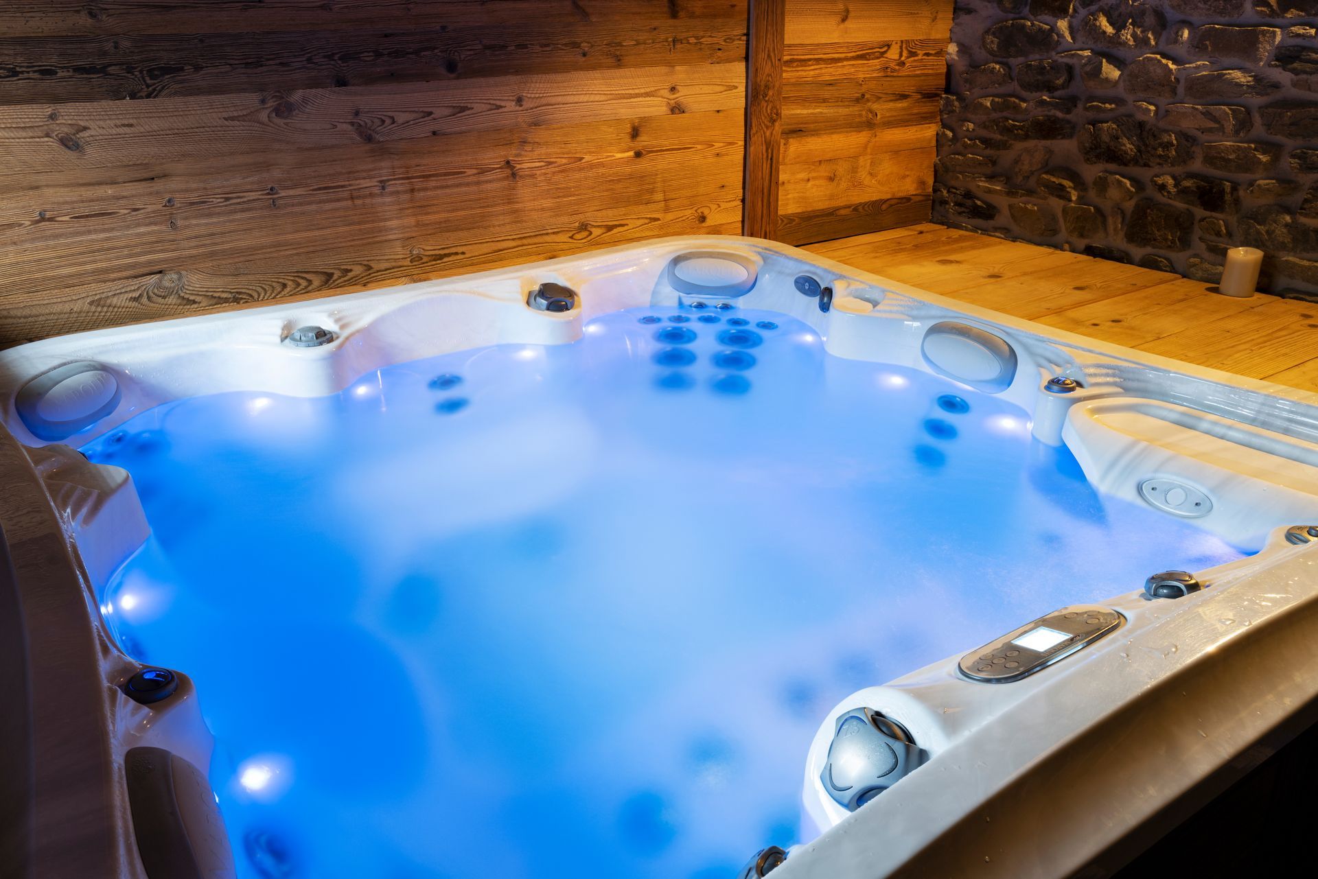 Lit blue hot tub in a rustic room with wooden and stone walls.