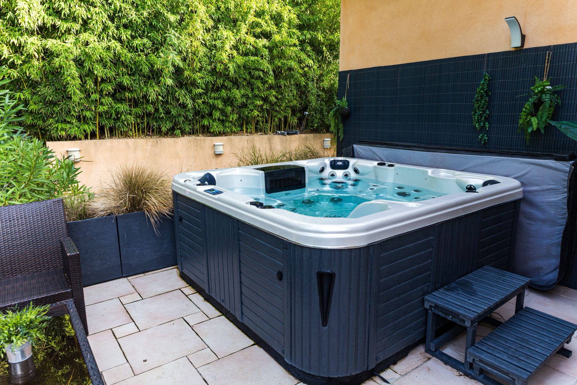 Hot tub on patio surrounded by greenery and black walls, with a two-step stool for entry.