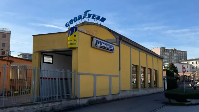 Un'officina meccanica luminosa con un'auto verde sollevata su un ponte idraulico e uno scooter blu parcheggiato sul pavimento di cemento.