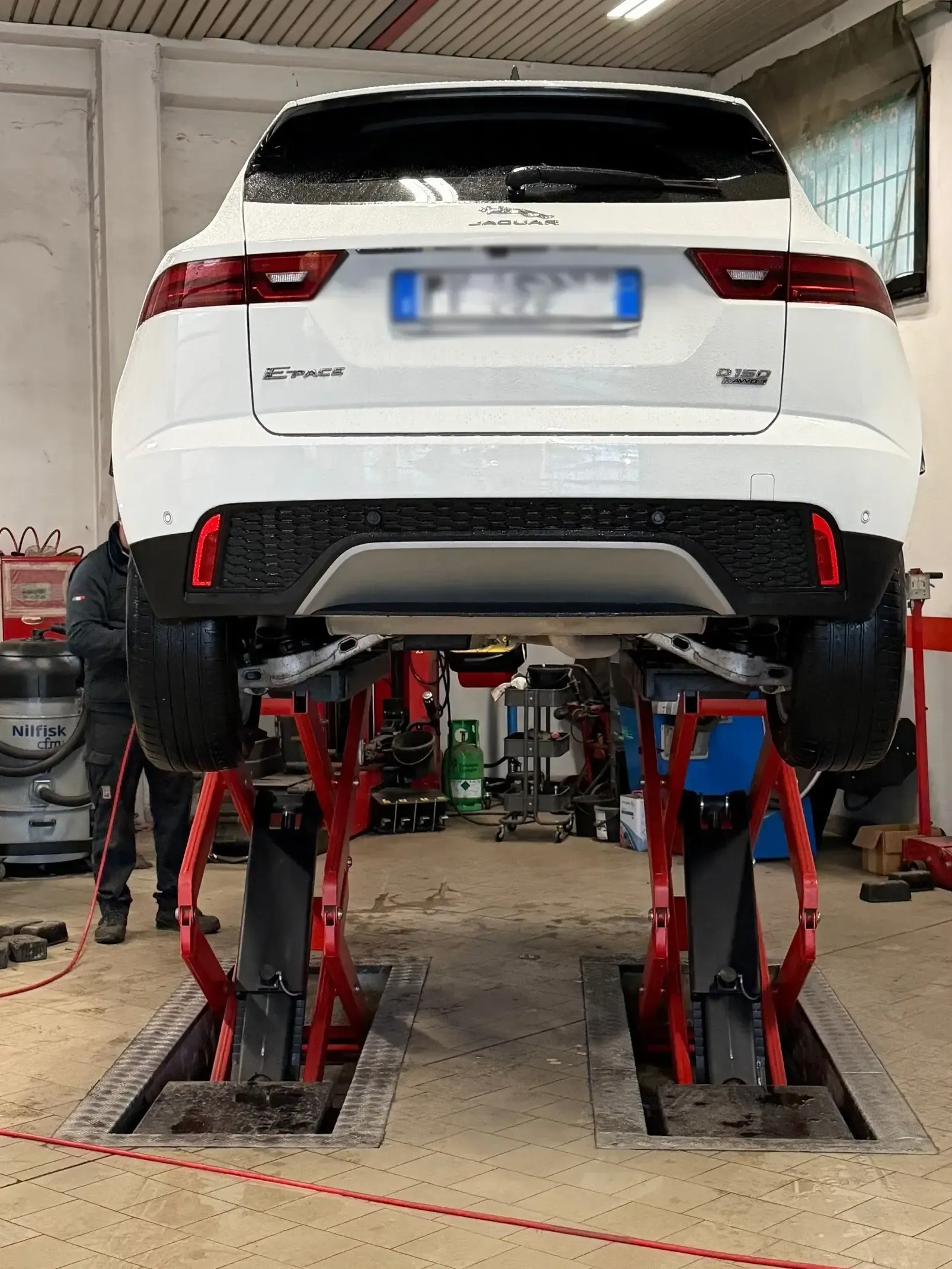 Un SUV bianco viene sollevato su un sollevatore idraulico a forbice rosso all'interno di un'officina meccanica.