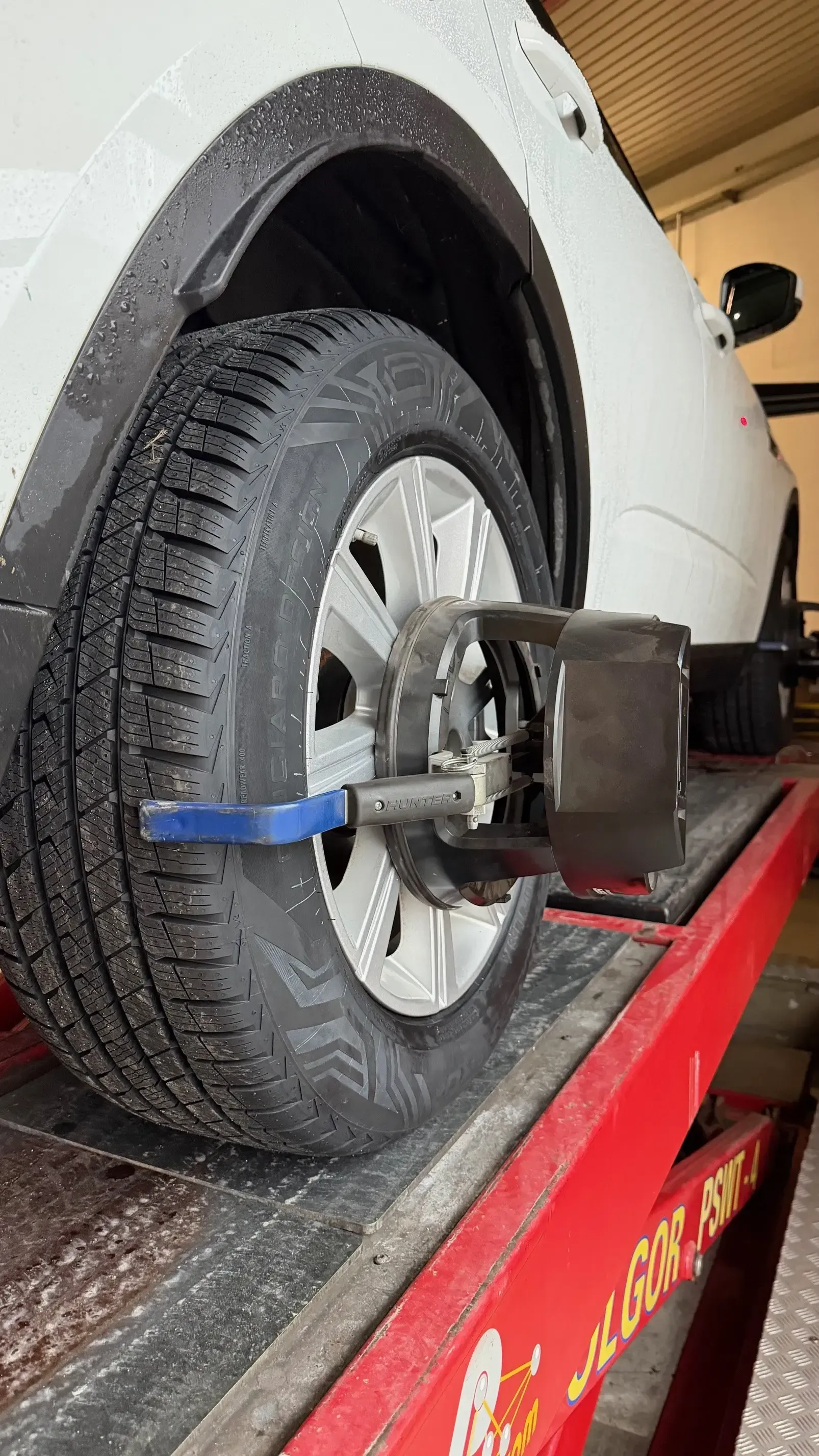 Un sensore di allineamento delle ruote è montato sul pneumatico anteriore di un'auto bianca parcheggiata su un ponte di servizio.