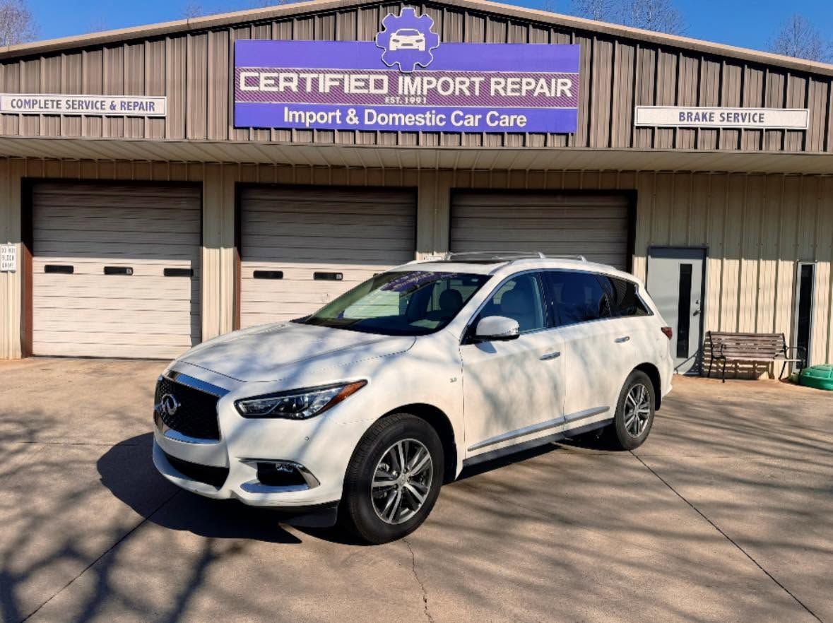White SUV parked outside Certified Import Repair shop with garage doors and sign above entrance | Certified Import Repair