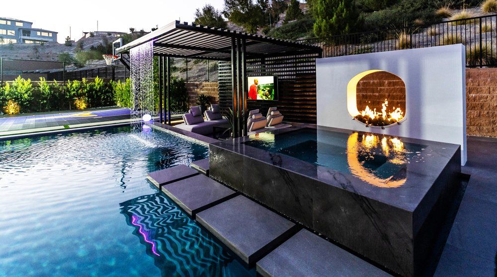 Custom swimming pool featuring a spa, fire features, sunken lounge area, rain descent, and basketball hoop. Pool project designed and built by Westmod. Custom swimming pool featuring a spa, fire features, sunken lounge area, rain descent, and basketball hoop. Pool project designed and built by Westmod.