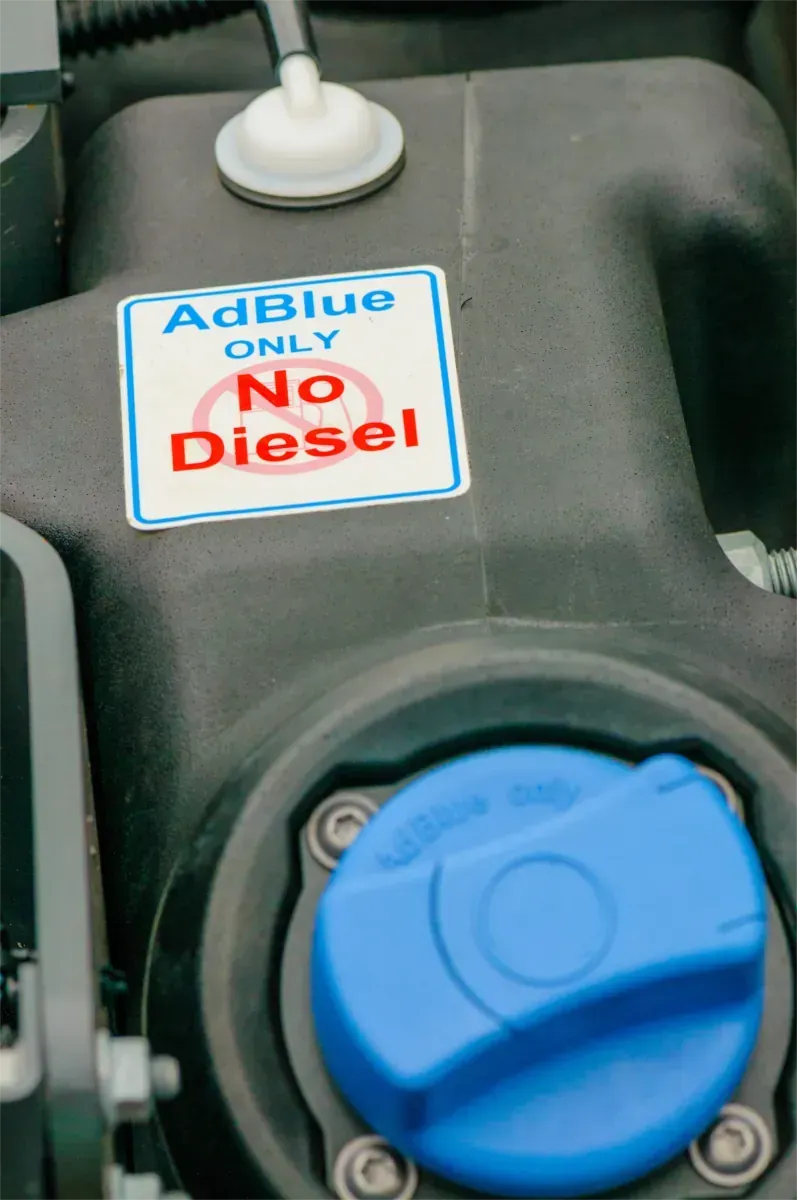 Blauer Dieseltankdeckel mit einem Aufkleber mit der Aufschrift „NUR AdBlue, kein Diesel“ auf einem Maschinentank.