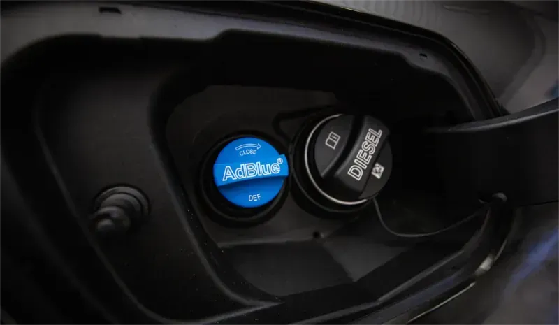 Nahaufnahme eines Autotankeinfüllstutzens mit blauem AdBlue-Verschluss und schwarzem Dieselverschlussverschluss hinter der geöffneten Tankklappe