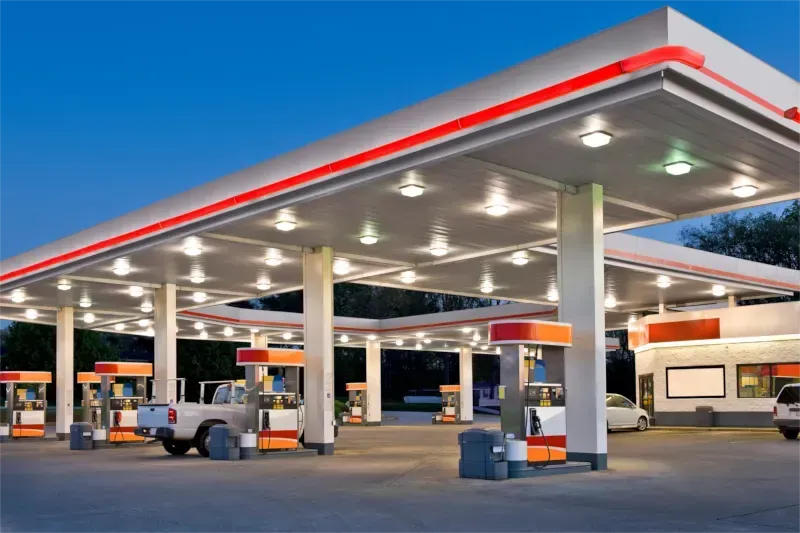 Tankstellenüberdachung in der Abenddämmerung mit geparkten Fahrzeugen und hellen Lichtern