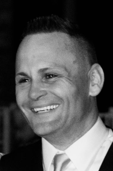 Ched H Peck smiling, with a high-fade haircut, wearing a suit and tie.