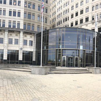 Exterior view of a modern building with a rounded glass entrance. Flags fly in front.