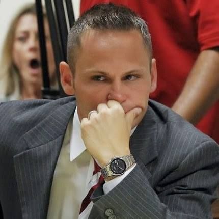 Man in suit looks thoughtful, touching his face. Woman in background appears surprised.