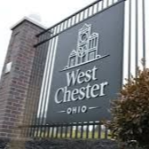 West Chester, Ohio sign with town emblem on a black background, set on a brick pillar.