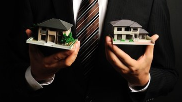 Man in suit holding miniature model houses, showcasing real estate options.