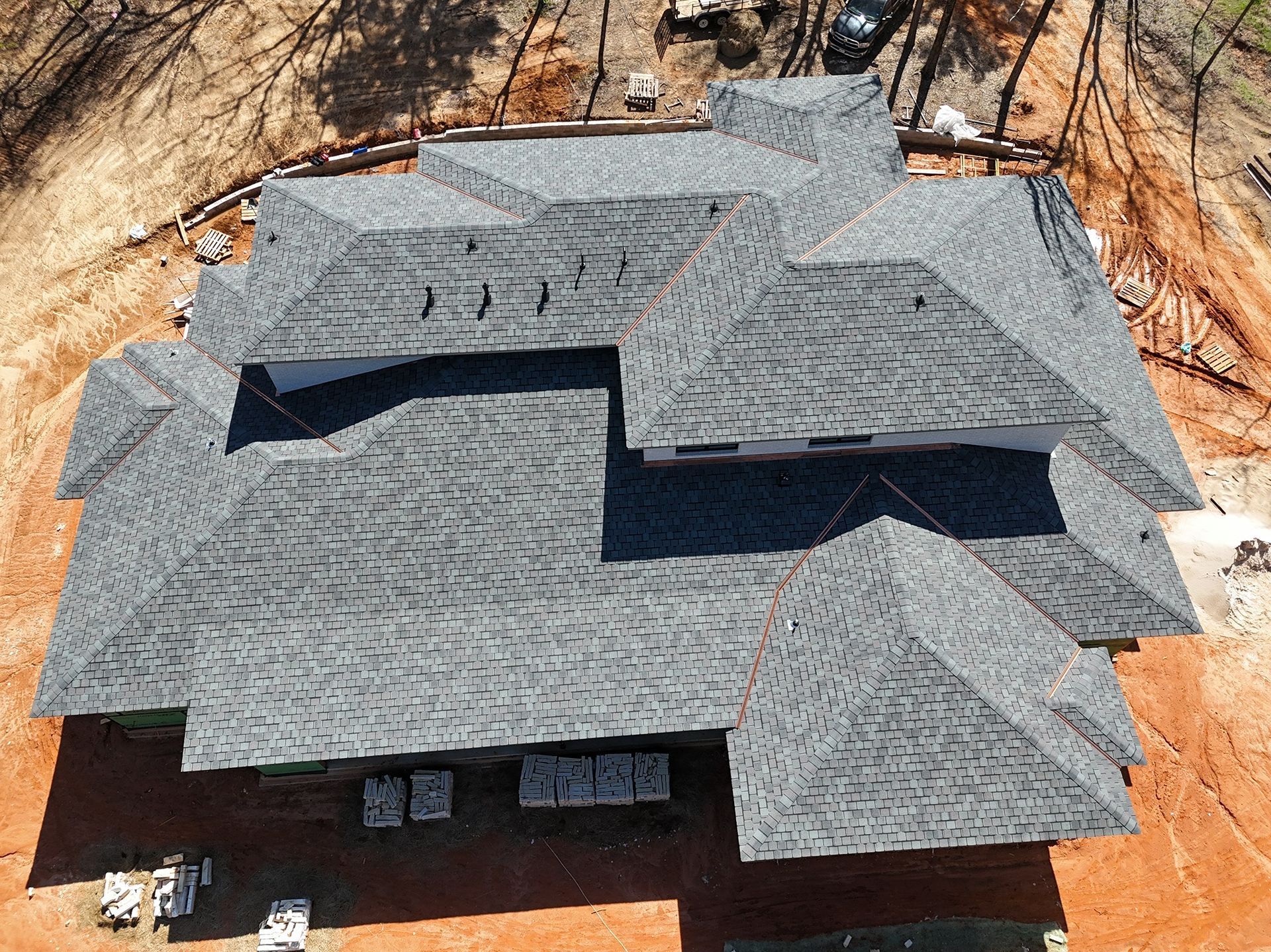 Aerial view of a gray shingled house roof under construction on a dirt lot