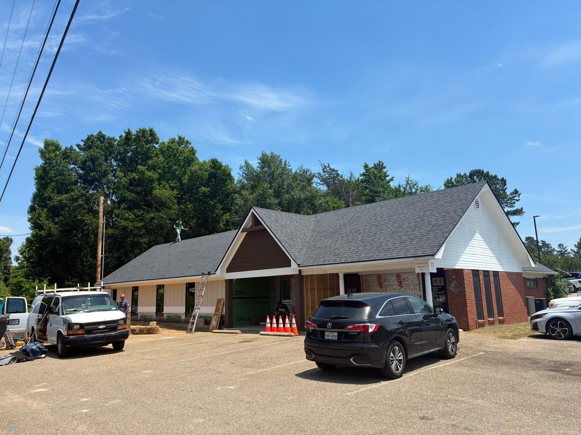 Small roadside building with parked cars and trees under a blue sky.