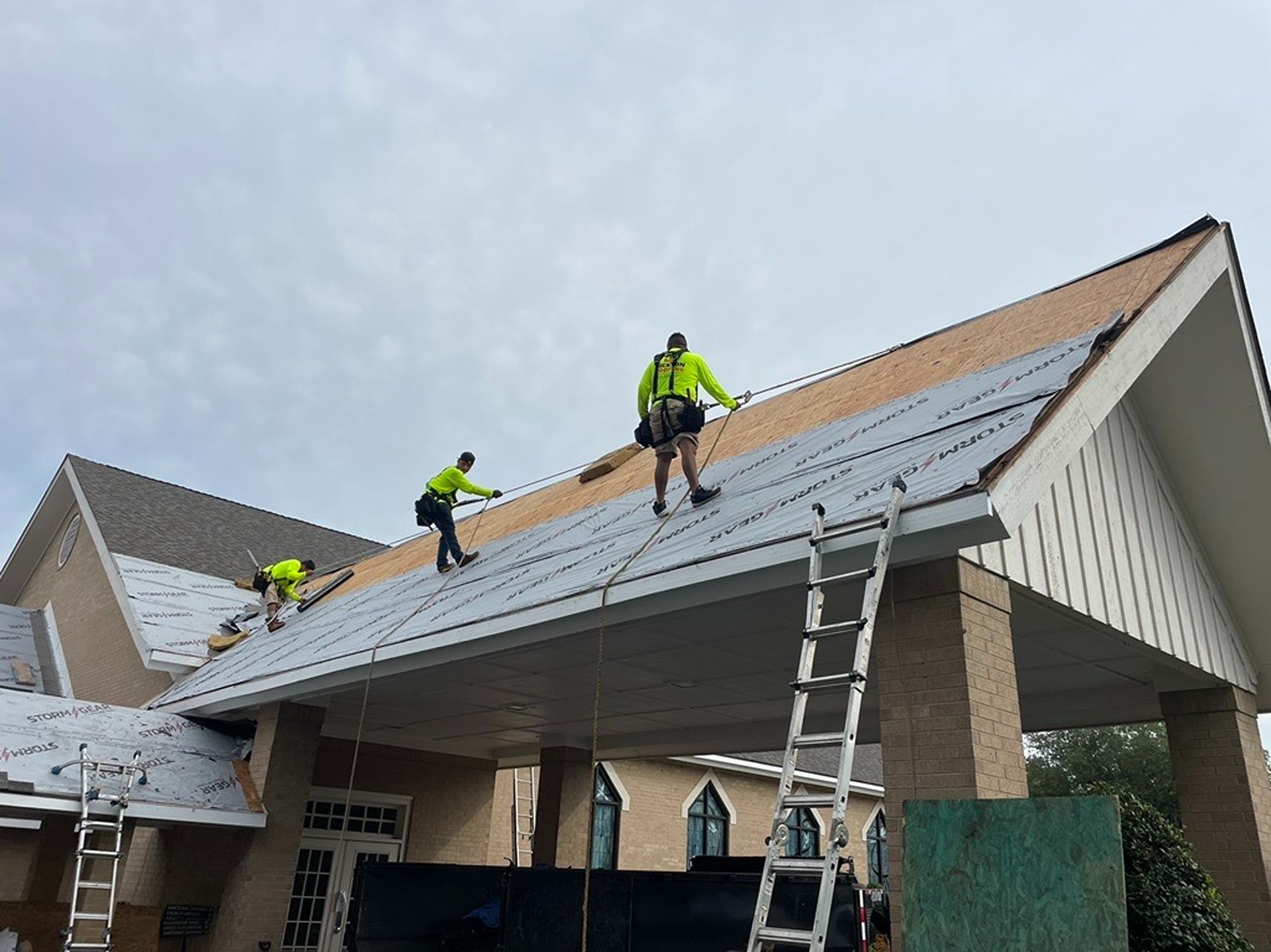 Workers installing solar panels on a house roof with a ladder under a cloudy sky