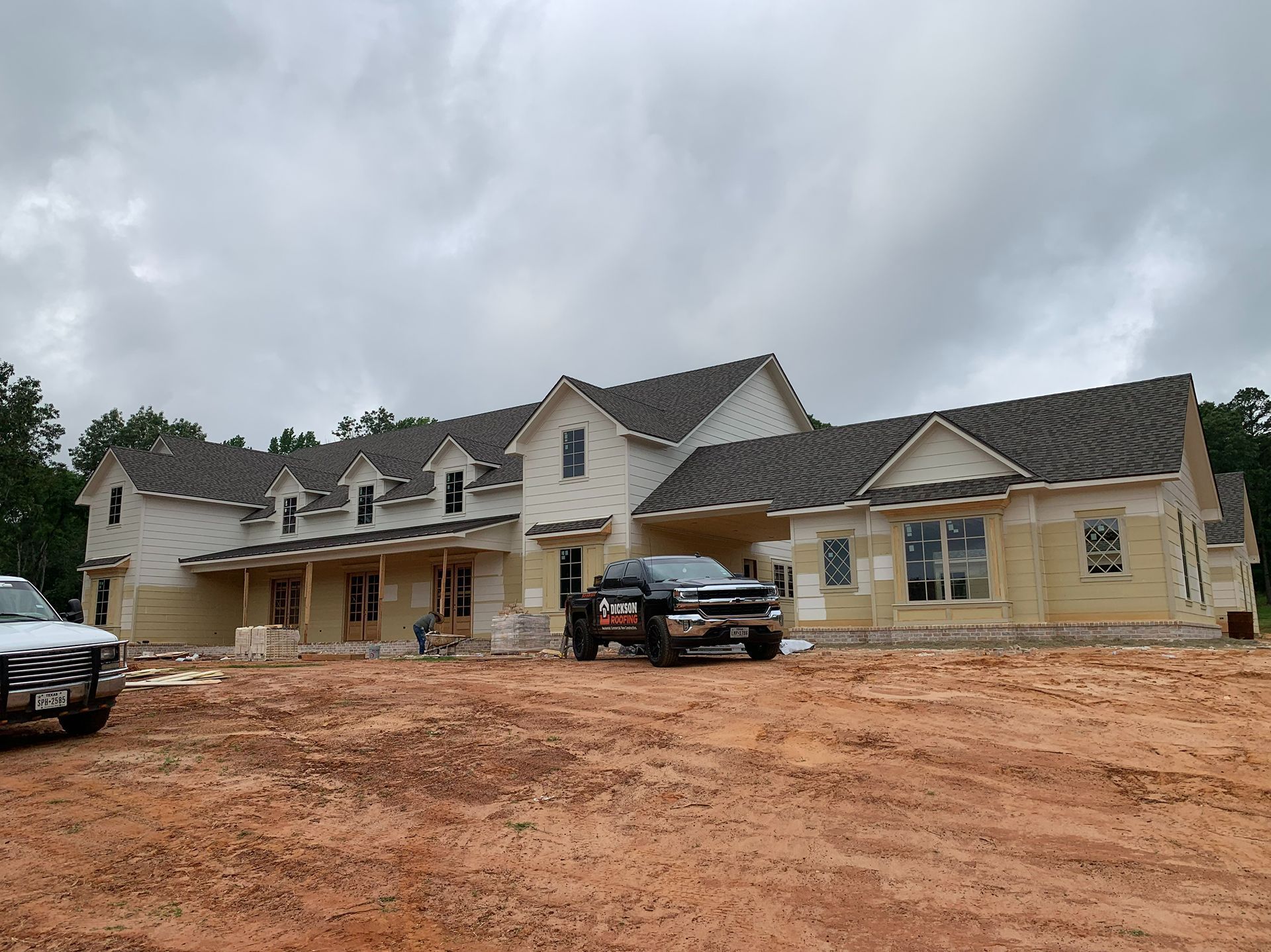 Large unfinished house with parked trucks on a muddy construction site under cloudy skies
