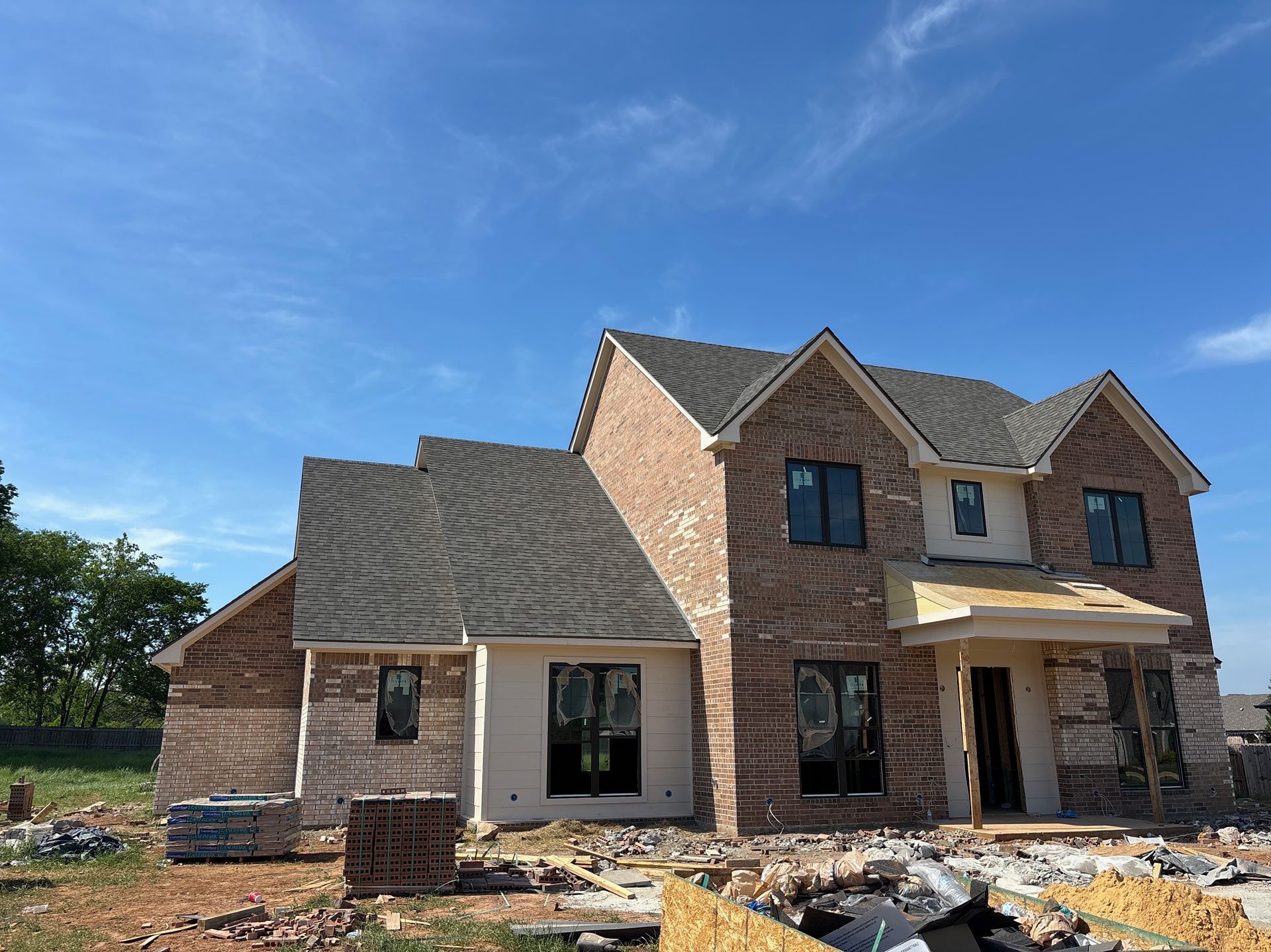 Two-story brick house under construction with exposed dirt yard and blue sky