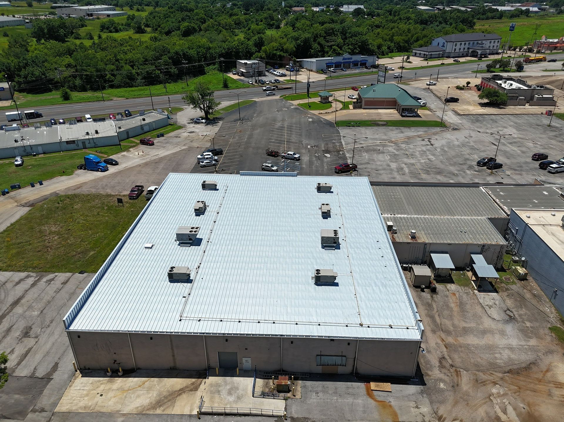Aerial view of a large white-roofed industrial building with nearby construction vehicles and dirt lots.