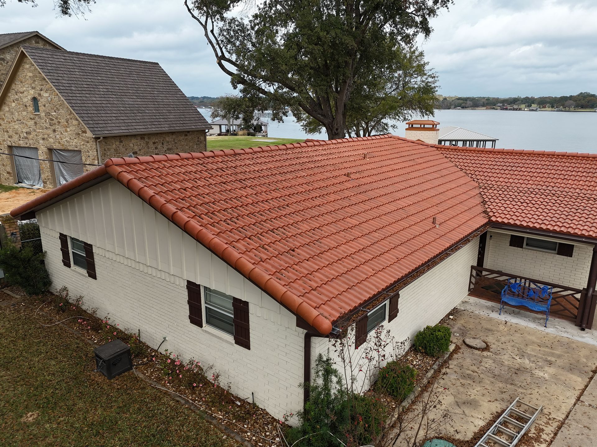 White house with red tile roof near the water, beside a stone building and trees