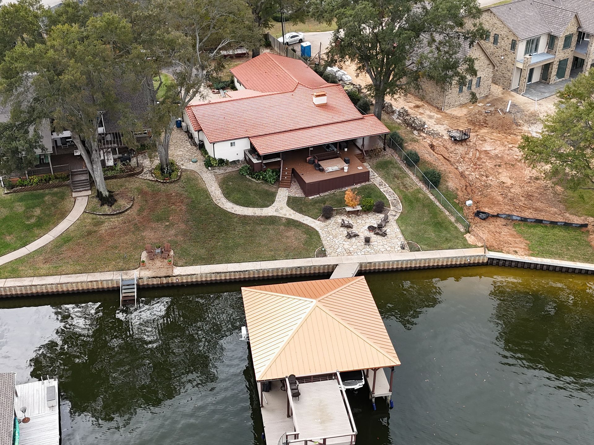 Aerial view of a lakeside house with a red roof, dock, and small pavilion by the water.
