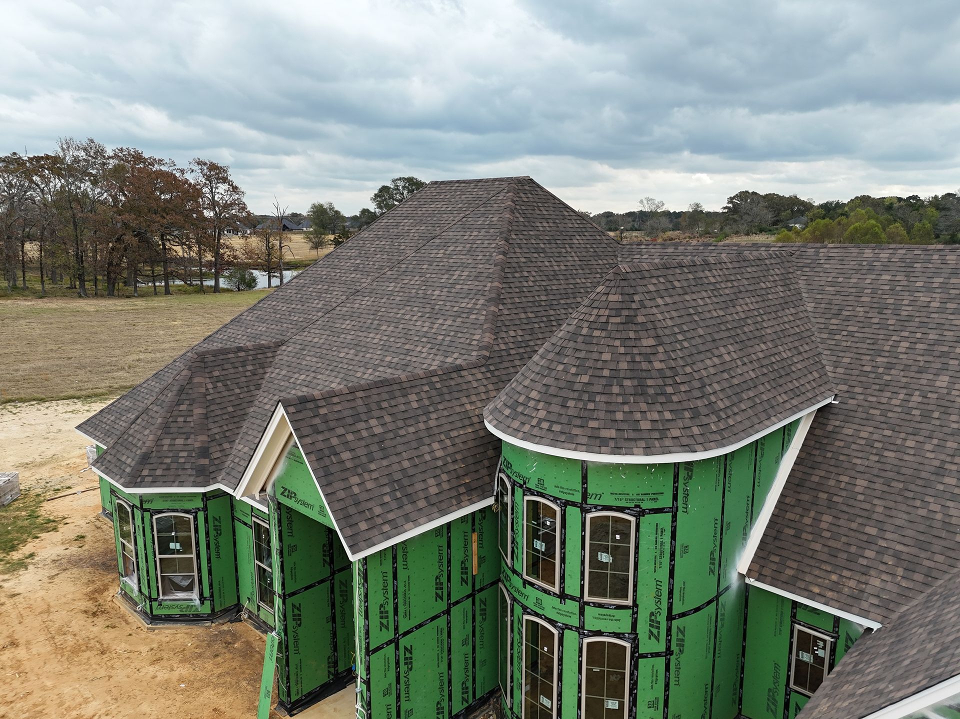 Green house with dark shingle roof and damaged exterior, viewed from above in a rural area