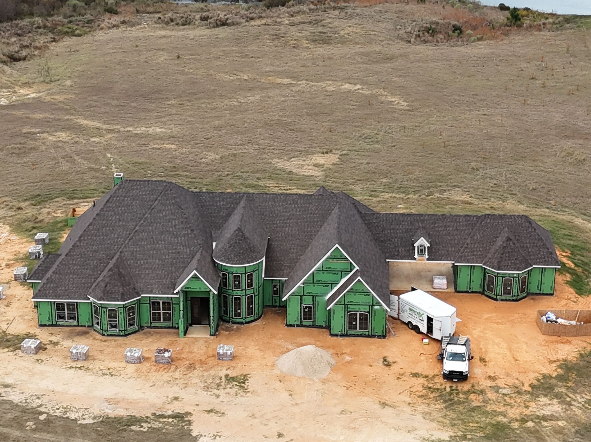 Aerial view of a large green house with black roof on a dusty construction site.