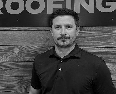 Man standing in front of a wood-paneled wall with partial “ROOFING” sign above him