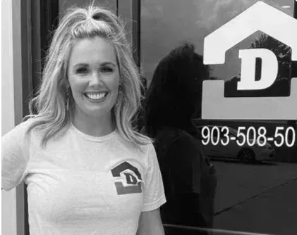 Smiling woman in a white T-shirt stands beside a window with a bold “D” logo and phone number.