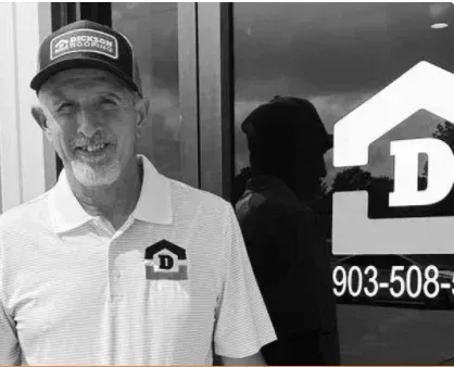 Man in baseball cap and polo shirt standing beside a glass door with a house logo and phone number.