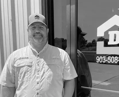 Man in a cap and short-sleeve shirt standing by a glass door with a logo and phone number.