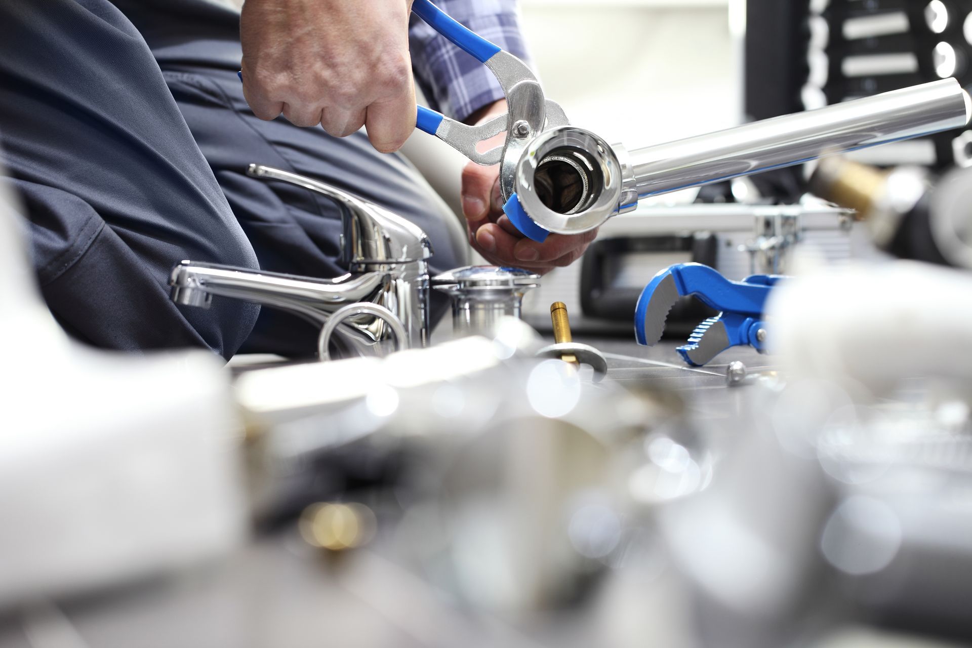 Plumber using blue pliers to assemble a faucet and plumbing parts in a work setting.