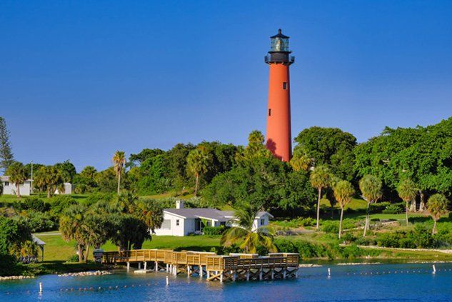 A red lighthouse is sitting on top of a lush green hill next to a body of water.
