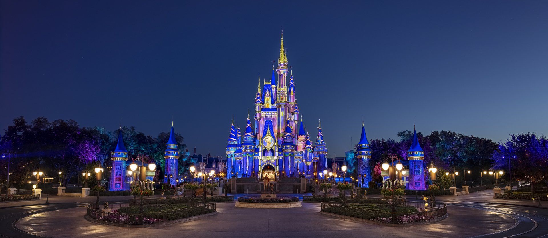 The disney castle is lit up at night with blue lights.