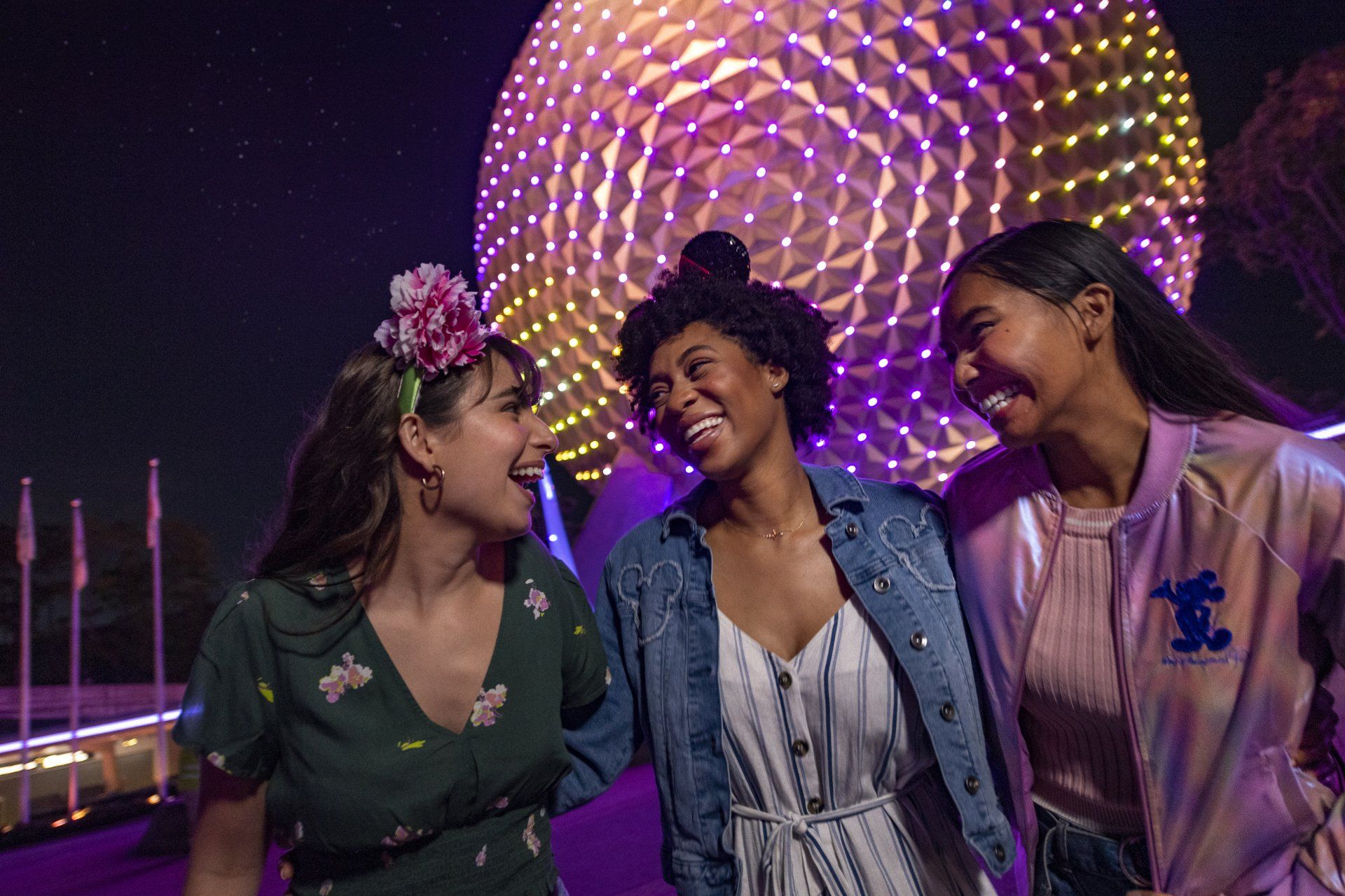 Three women are standing next to each other in front of a purple building.