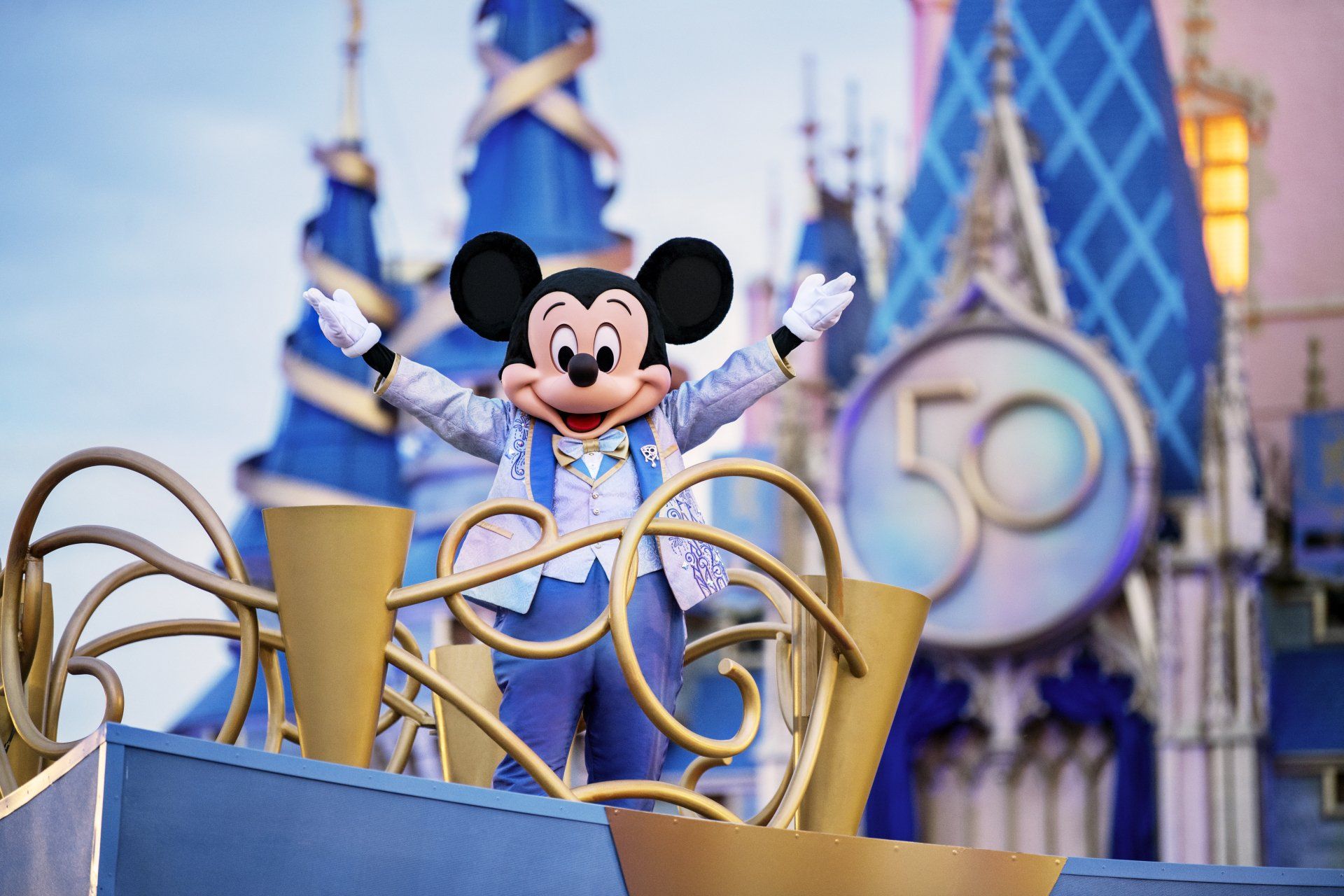 Mickey mouse is standing on a float in front of a castle.